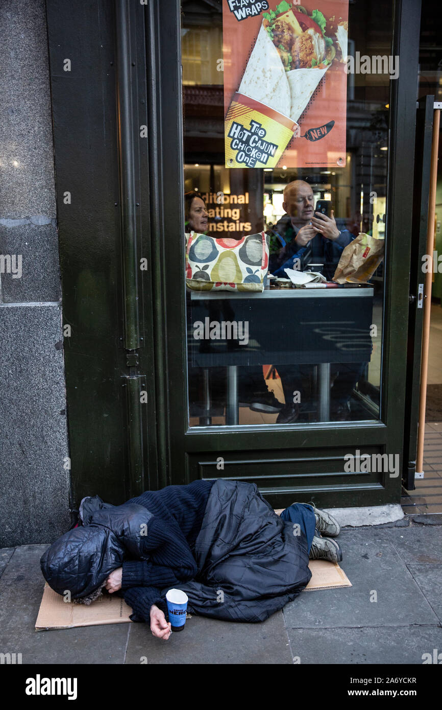 Rauer Schlaf liegt auf der Straße außerhalb einer Fast-Food-Kette, während die Menschen im Inneren der warmen Speisen am Fenster, Central London, Großbritannien sitzen Stockfoto