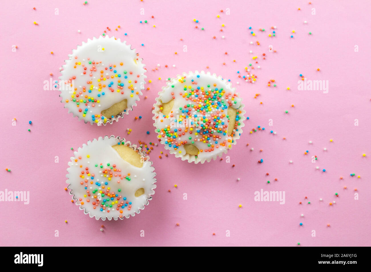 Drei kleine weiße Milchglas cupcakes in der Mitte der rosa Hintergrund bestreut mit bunten Streuseln auf Rosa mit Kopie Raum Stockfoto