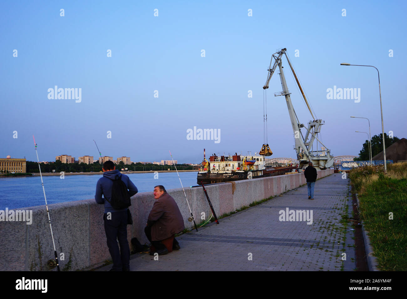 Zwei Angler am Ufer der Newa, hinten Entladen von Kohle von einem Flussfrachter, Ufer der Newa, Sankt Petersburg, Russland Stockfoto