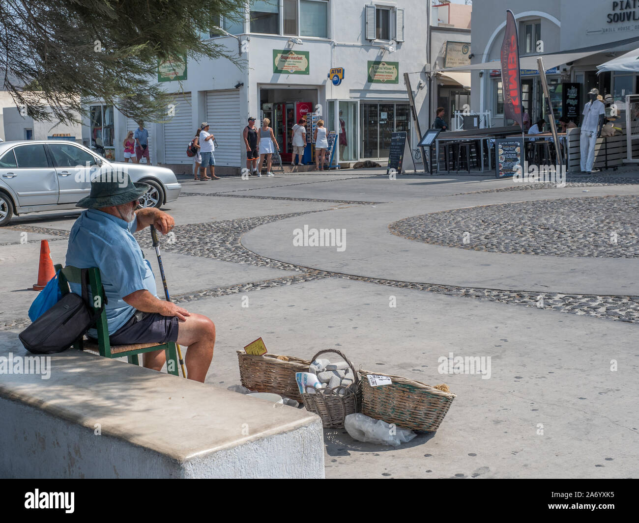 Einem Straßenhändler Standortwahl auf Stuhl verkauf Bimsstein in Körben in Mitte Mitte Pflastersteine gemusterten Design Platz des Dorfes Stadt Oia Santorini Stockfoto