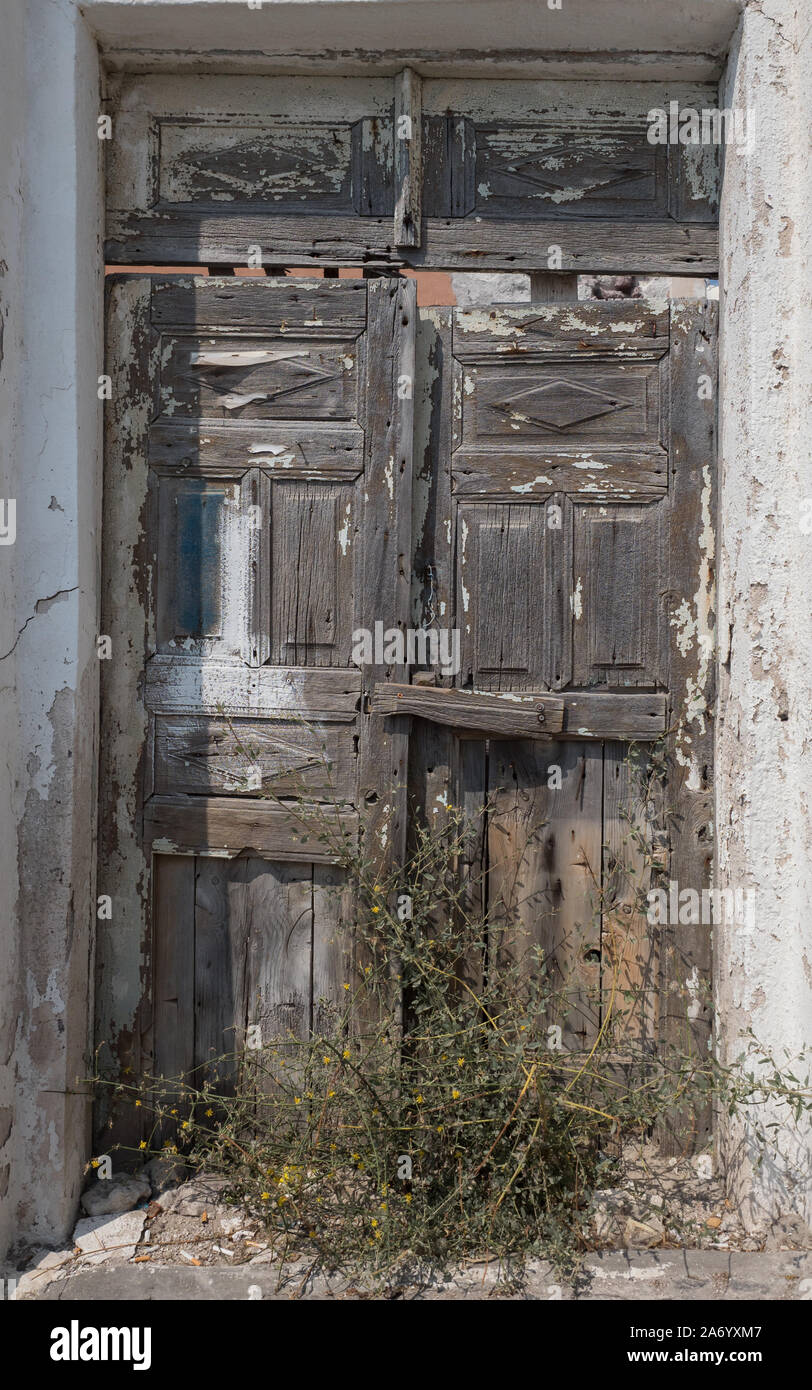 Ein verfallenes alten alten verlassenen vordere Tür in Tür weg Holz abblätternde Farbe wachsende Unkraut anlage Oia Santorini Stockfoto