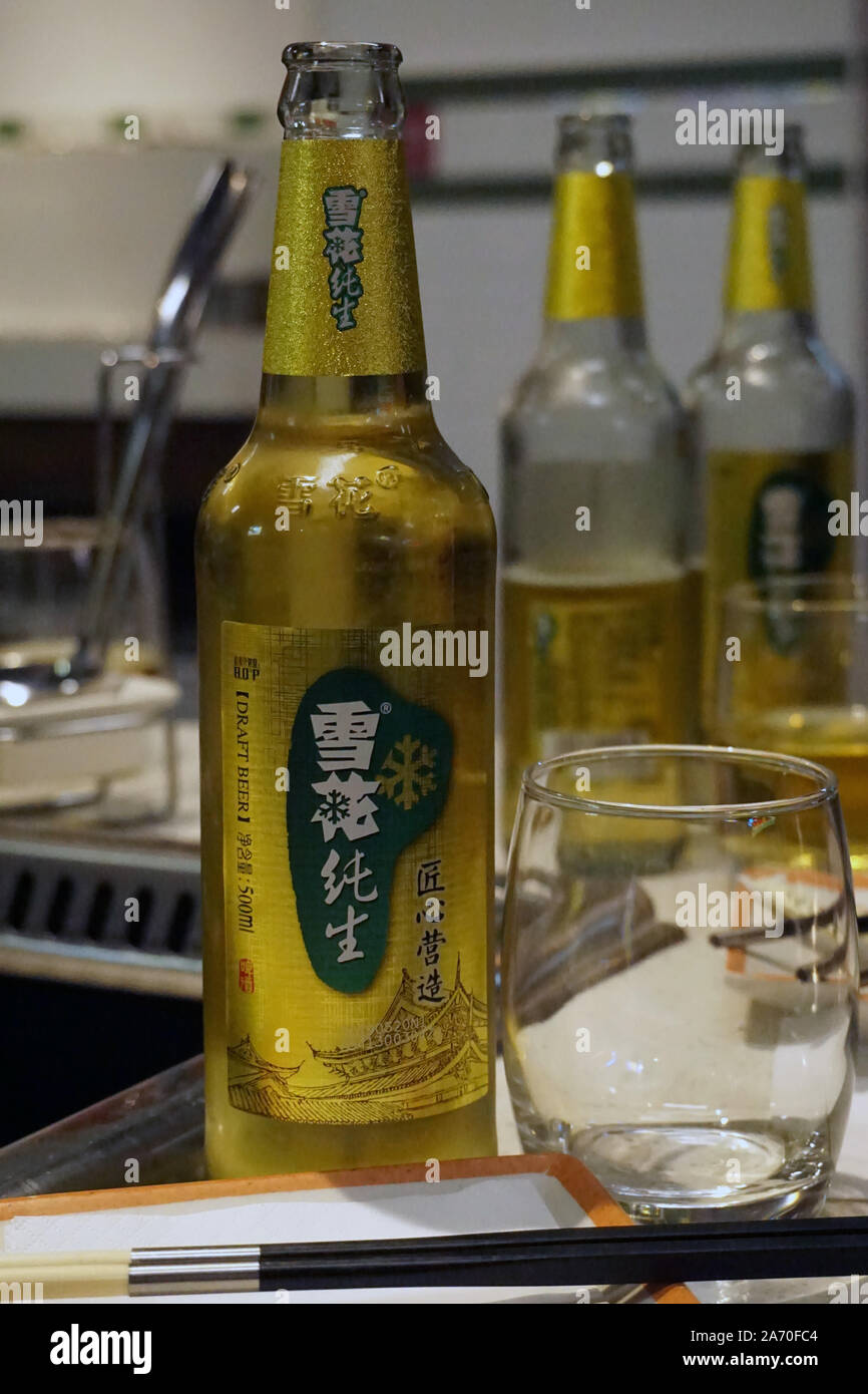 Tsingtao Bier Nummer 9 in einer grünen Flasche mit der Hälfte-gefüllt hohes Glas Bier mit einem Kopf Stockfoto