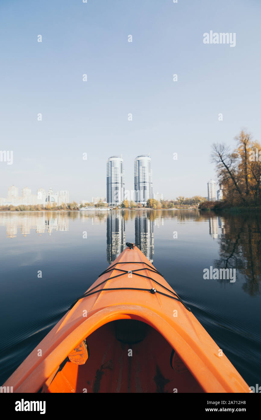 Orange Kajak Nase segeln auf modernen Gebäuden auf den Gewässern des Dnipro River in Kiew, Ukraine. Vertikale Ausrichtung Stockfoto