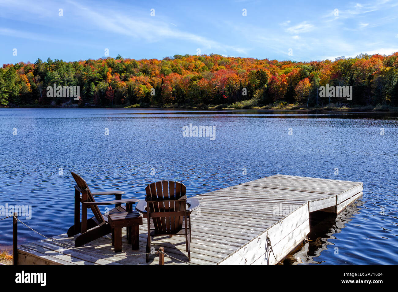 Zwei Muskoka Stühlen sitzen auf einem Holz Dock mit Blick auf einen See in einer ruhigen Herbst an einem sonnigen Tag Stockfoto