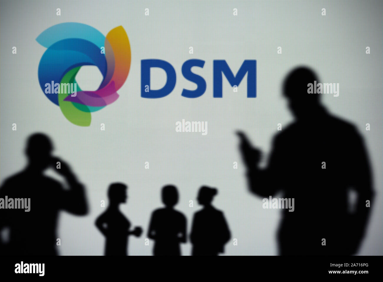 Die DSM-Logo ist auf einen LED-Bildschirm im Hintergrund, während eine Silhouette Person ein Smartphone verwendet (nur redaktionelle Nutzung) Stockfoto