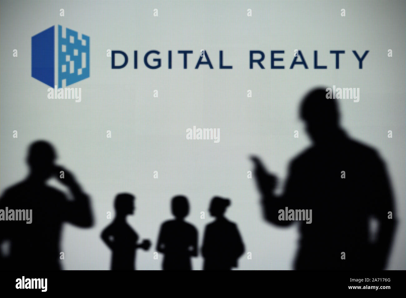 Die Digital Realty Logo ist auf einen LED-Bildschirm im Hintergrund, während eine Silhouette Person ein Smartphone verwendet (nur redaktionelle Nutzung) Stockfoto