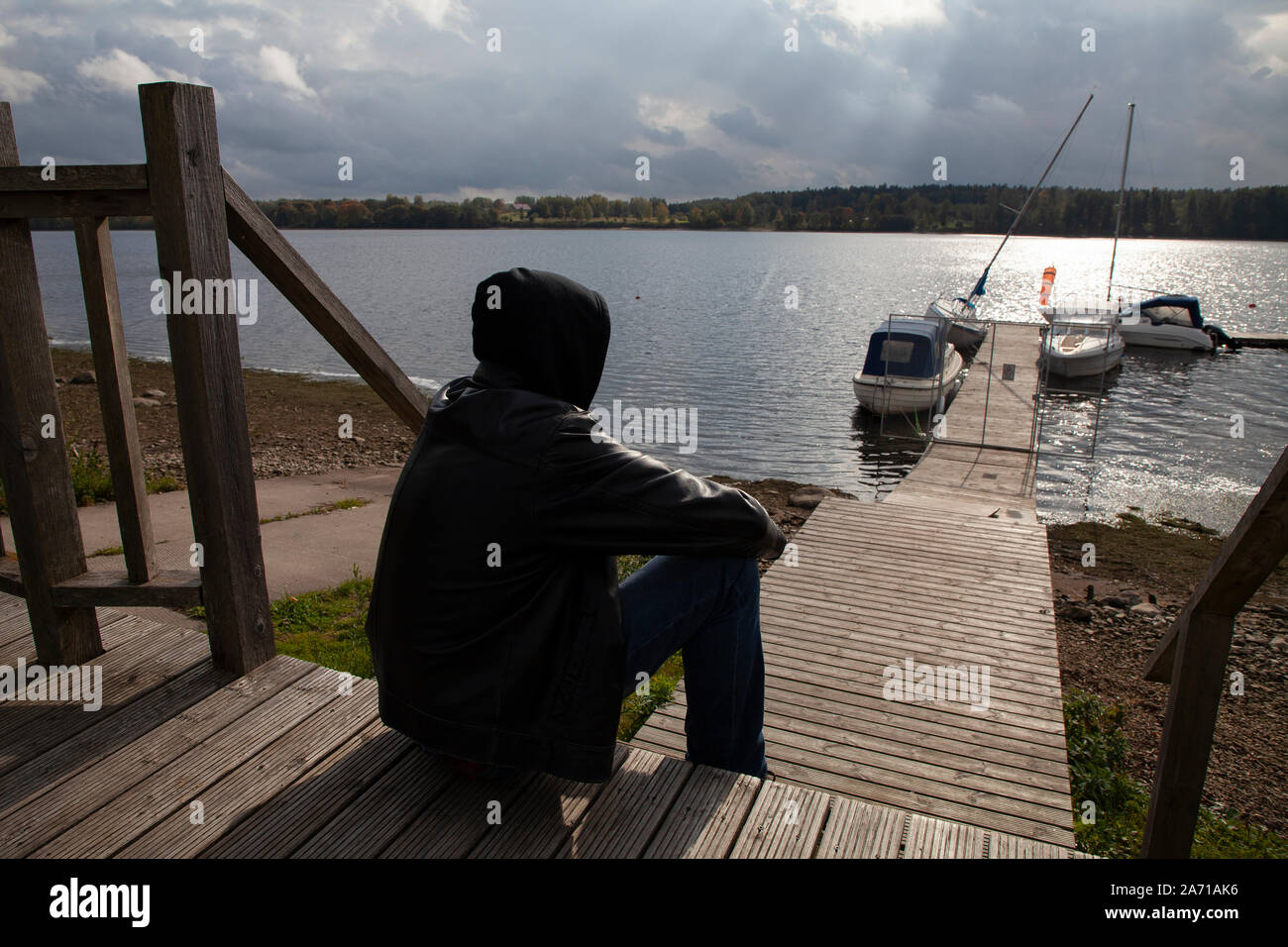 Konzeptionelle Bild eines einsamen Mann sitzt auf einem Flußufer und Blick auf die Boote und Yachten. Sieht aus wie er denkt oder Leiden Stockfoto