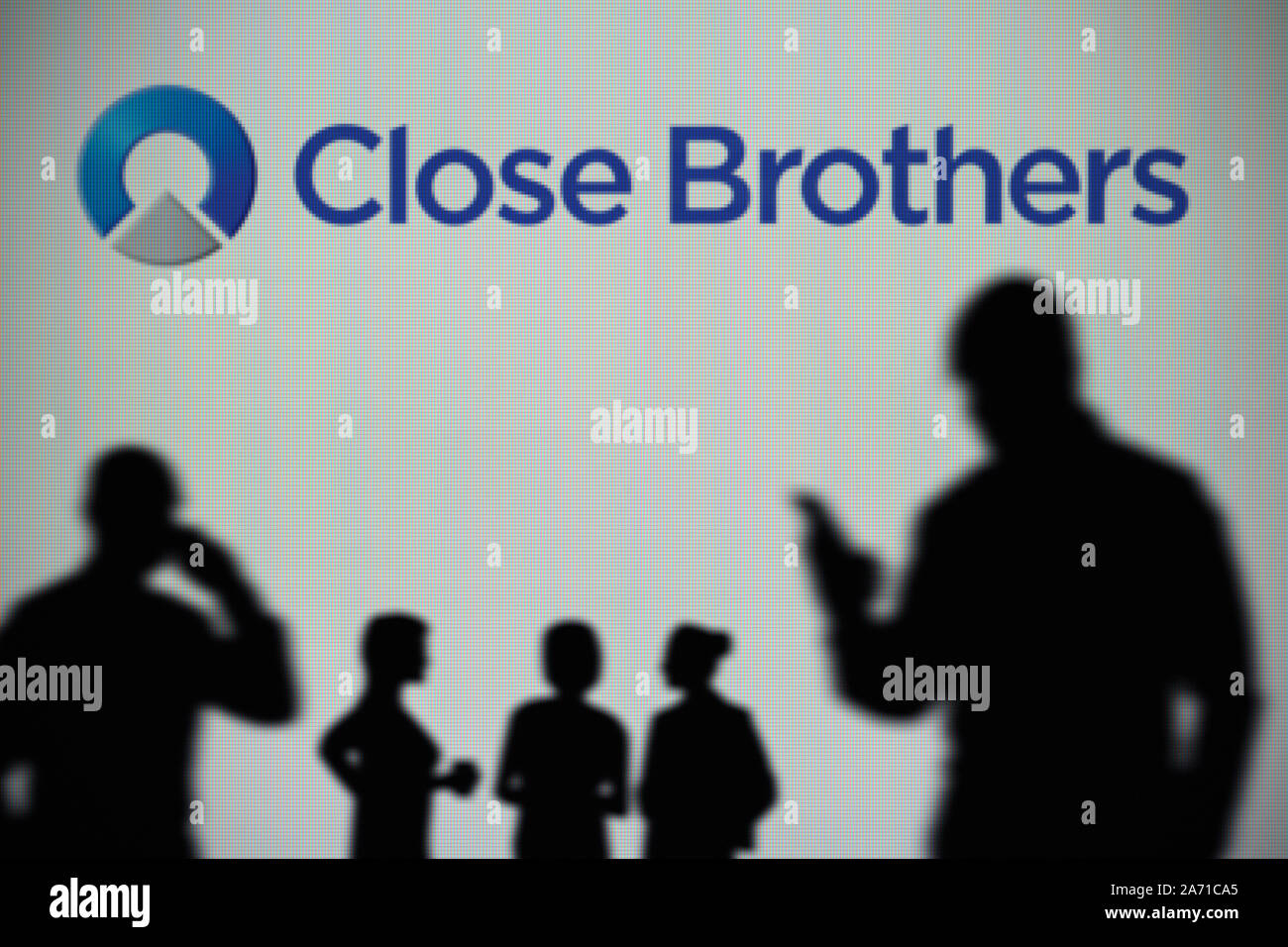 Die Close Brothers Group Logo ist auf einen LED-Bildschirm im Hintergrund, während eine Silhouette Person ein Smartphone verwendet (nur redaktionelle Nutzung) Stockfoto