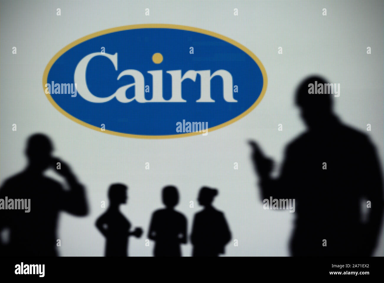 Der Cairn Energy Logo ist auf einen LED-Bildschirm im Hintergrund, während eine Silhouette Person ein Smartphone verwendet (nur redaktionelle Nutzung) Stockfoto
