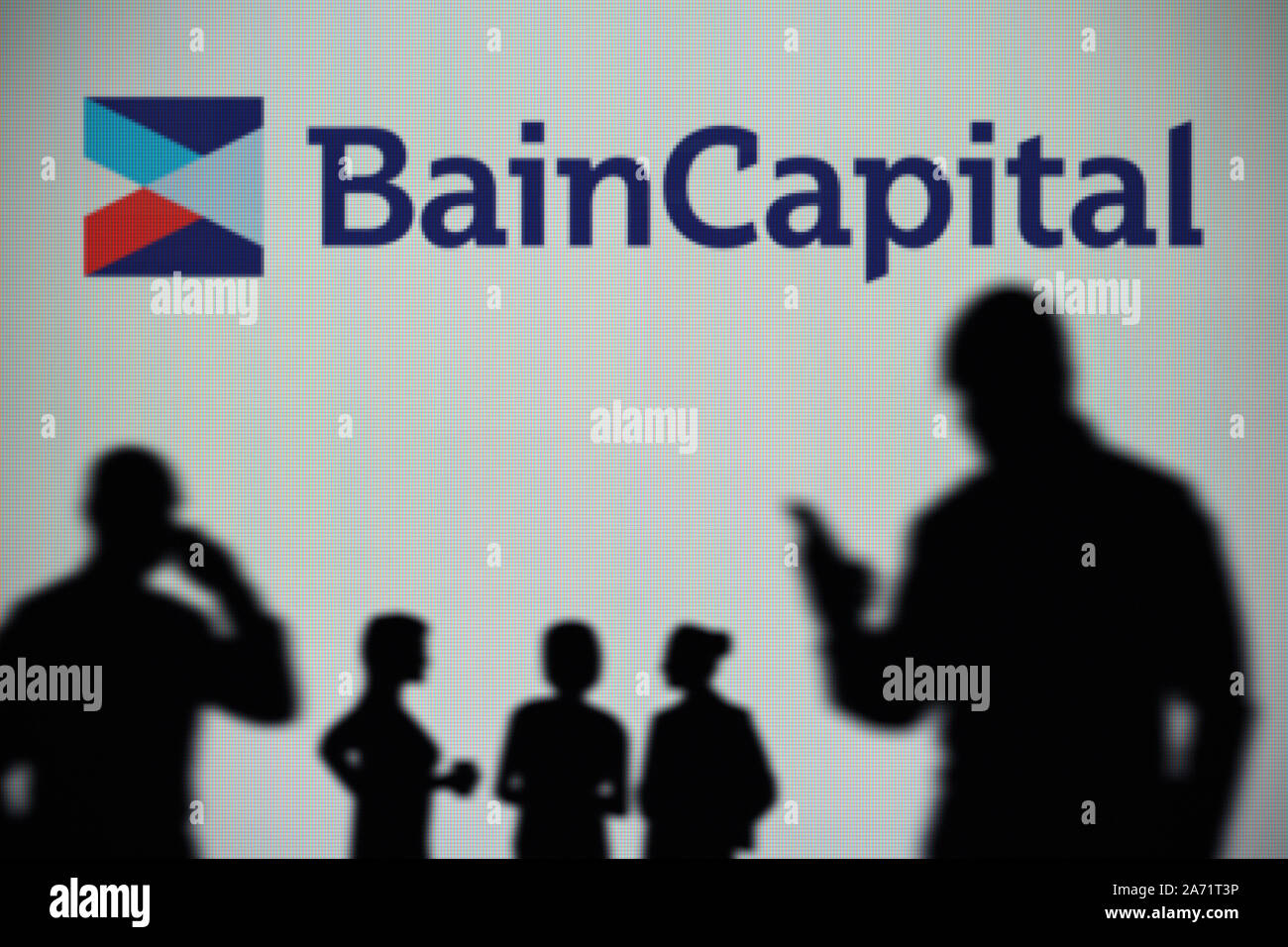 Die Bain Capital Logo ist auf einen LED-Bildschirm im Hintergrund, während eine Silhouette Person ein Smartphone verwendet (nur redaktionelle Nutzung) Stockfoto