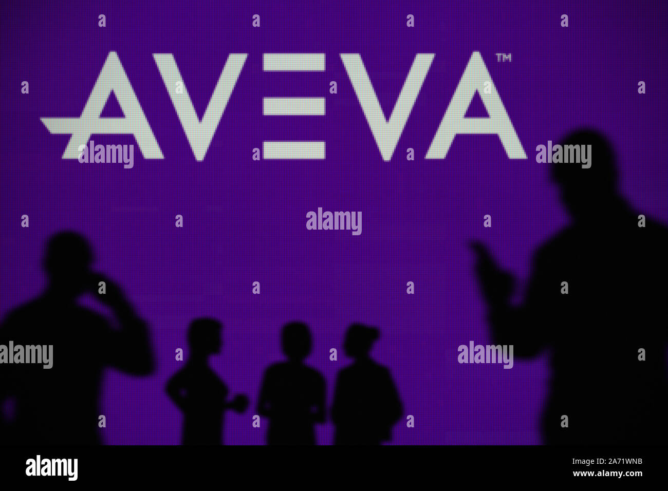 Die AVEVA-Logo ist auf einen LED-Bildschirm im Hintergrund, während eine Silhouette Person ein Smartphone verwendet (nur redaktionelle Nutzung) Stockfoto