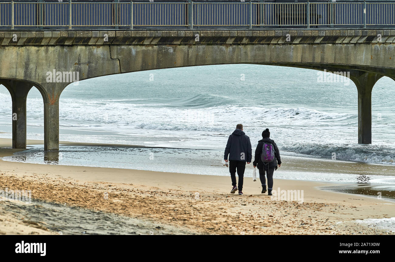 Paar am Strand entlang am Ufer unter der Pier von Bournemouth, England. Stockfoto