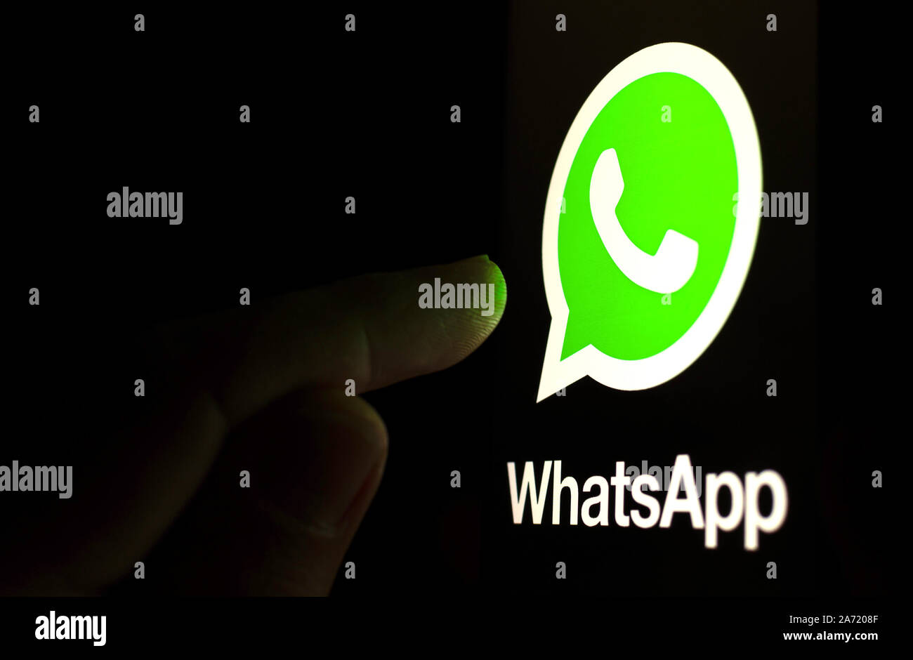 WhatsApp Logo auf dem Bildschirm des Smartphones in einem dunklen Raum und mit dem Finger auf sie zeigen. Stockfoto