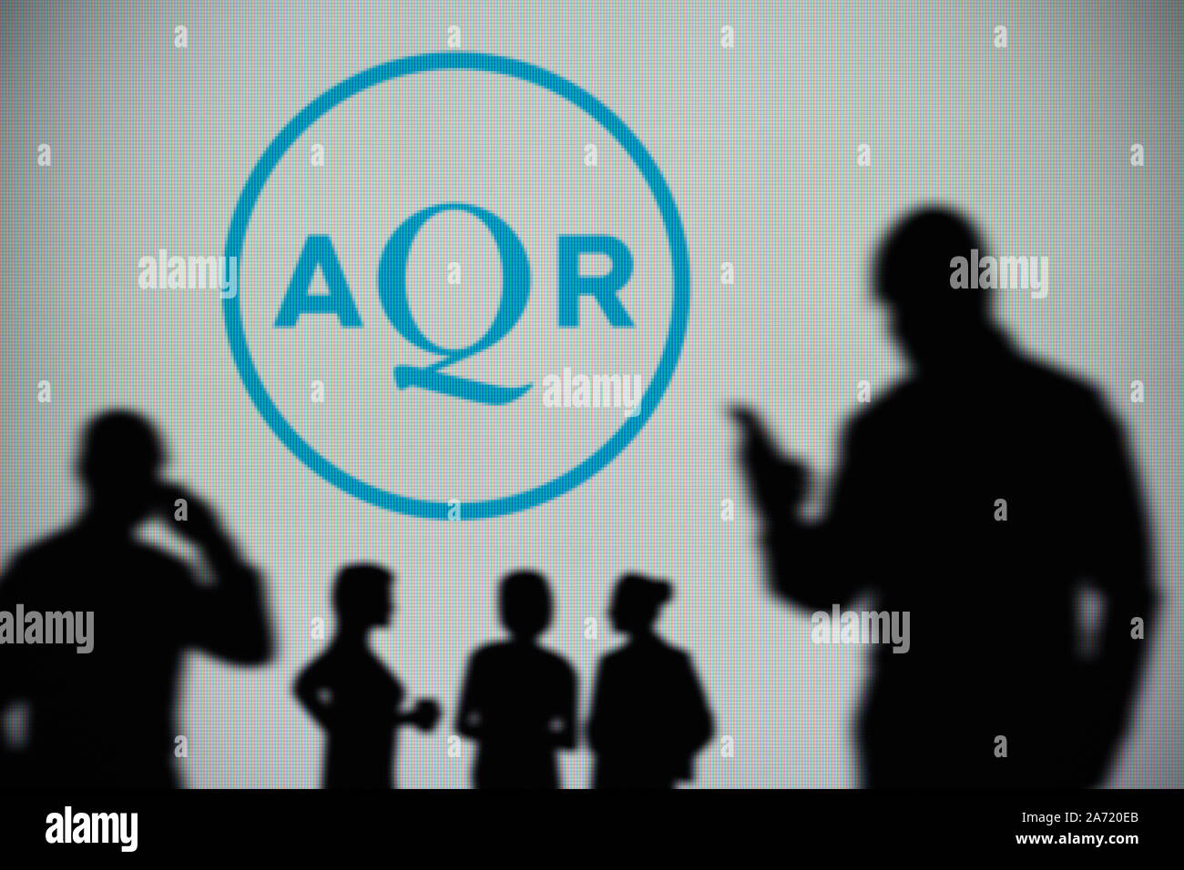 Die aqr Capital Management Logo ist auf einen LED-Bildschirm im Hintergrund, während eine Silhouette Person ein Smartphone verwendet (nur redaktionelle Nutzung) Stockfoto