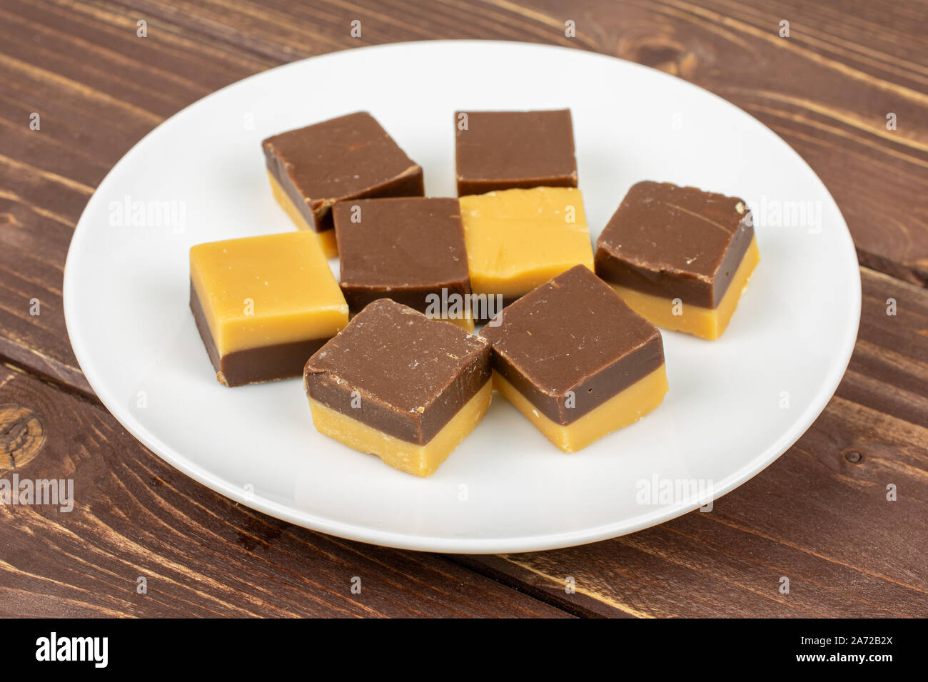 Gruppe der Acht ganze süsse braune Karamell Schokolade Süßigkeiten auf weißer Keramik Platte auf braunem Holz Stockfoto