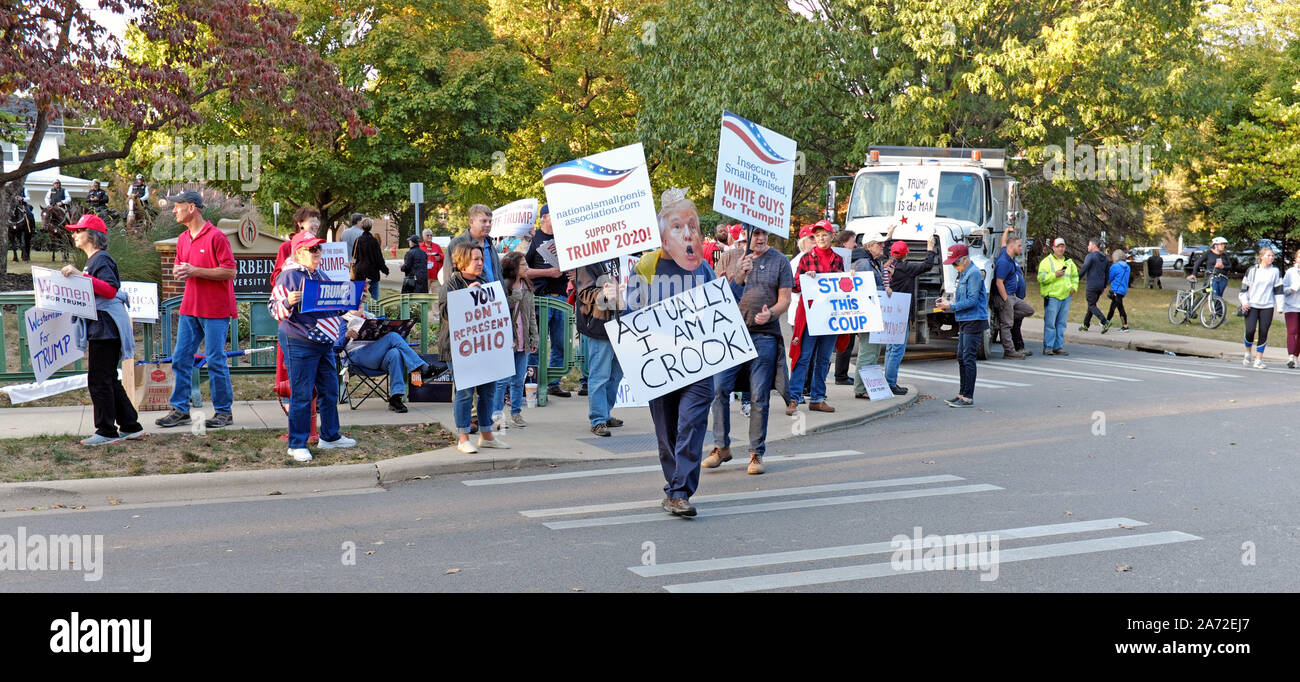 Trump-Anhänger in Westerville, Ohio, USA, halten Zeichen, die den präsidenten unterstützen, während ein Protestler spaziert, indem er ihn als Krämer anruft. Stockfoto