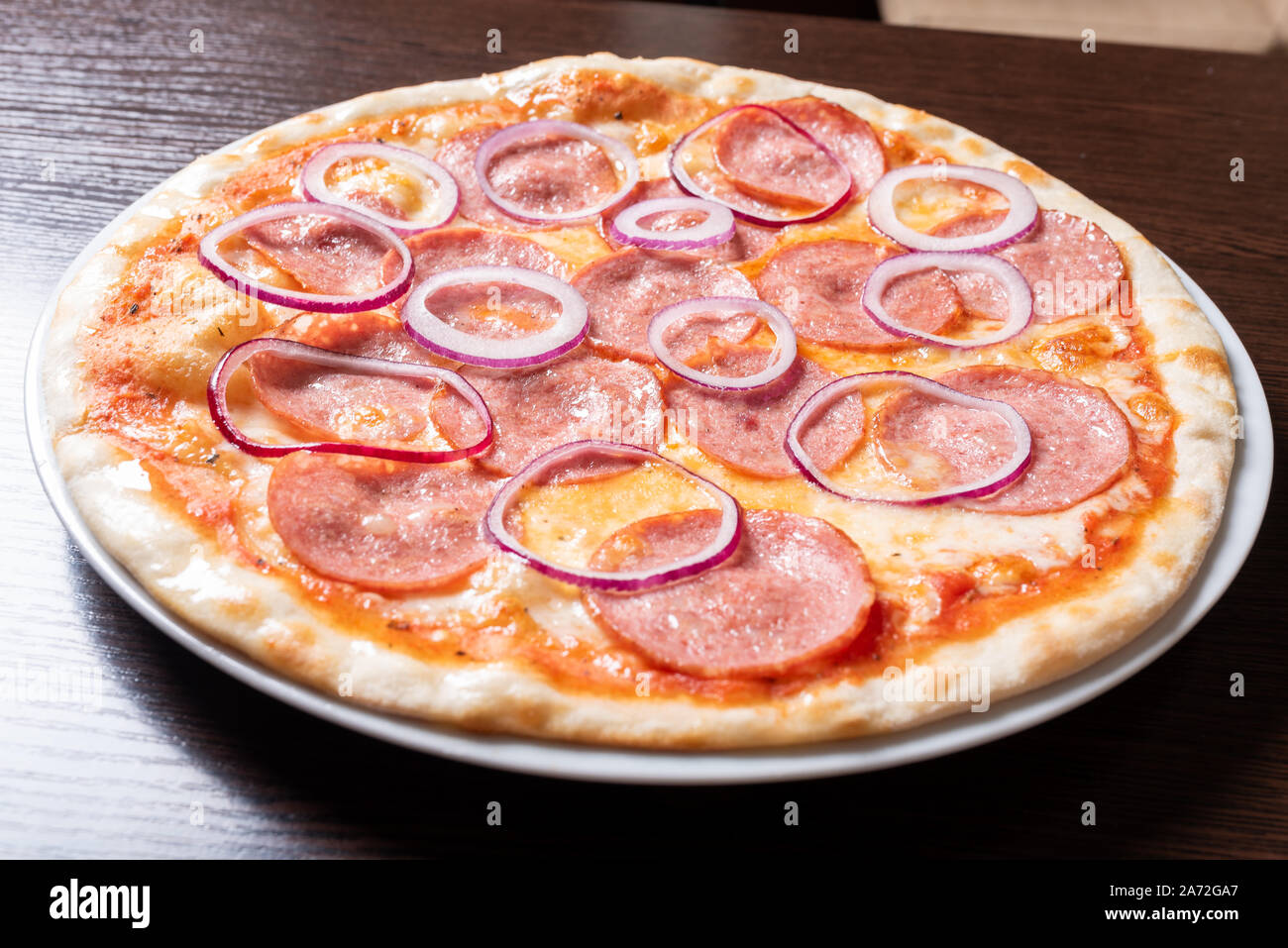 Billige Pizza mit Salami, Zwiebeln, in Tomatensauce. Stockfoto