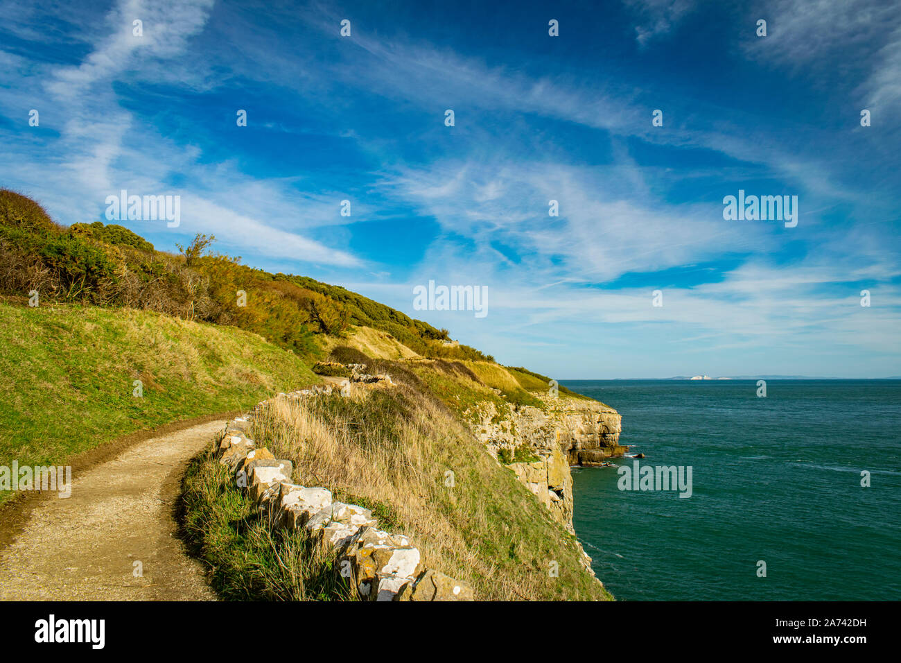 Küstenweg führt zu Anvil Point Lighthouse mit Steinmauer, Felsen und Meer an einem sonnigen Tag, Teil der Jurassic Coast, Swanage, Dorset, England Stockfoto