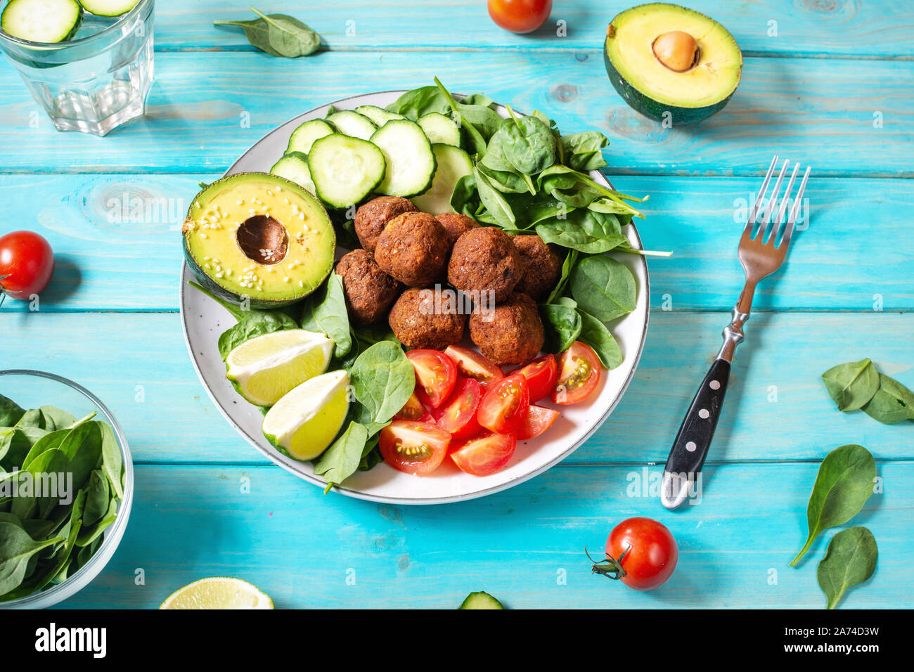 Salat mit Avocado, Falafel, Gurke, Cherry Tomaten und Spinat auf Blau Holz Hintergrund. Gesund vegan Mittagessen Schüssel Stockfoto