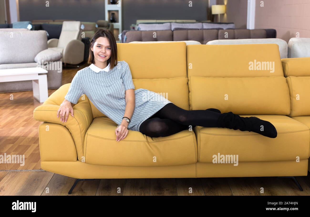 Porträt der jungen fröhliche Frau Prüfung gelb Sofa im Möbel Shop Stockfoto
