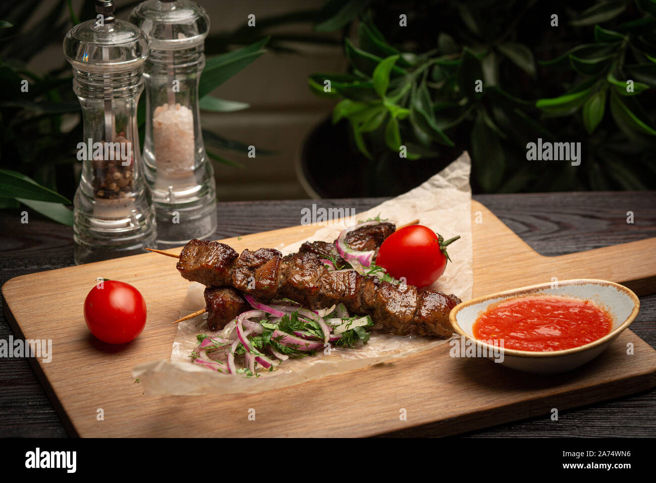 Lamm am Spieß mit eingelegten Zwiebeln und Koriander auf einem Holzbrett und Ketchup in einer Schale auf einem dunklen Hintergrund Stockfoto