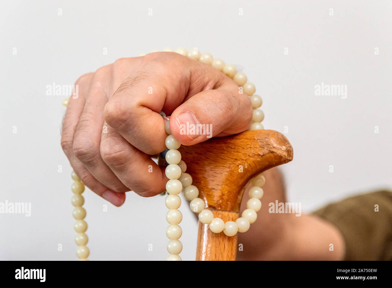 Nahaufnahme der männlichen Hand mit einem Spazierstock Holding beten Perlen auf weißem Hintergrund. Behinderung und glauben Konzept. Stockfoto