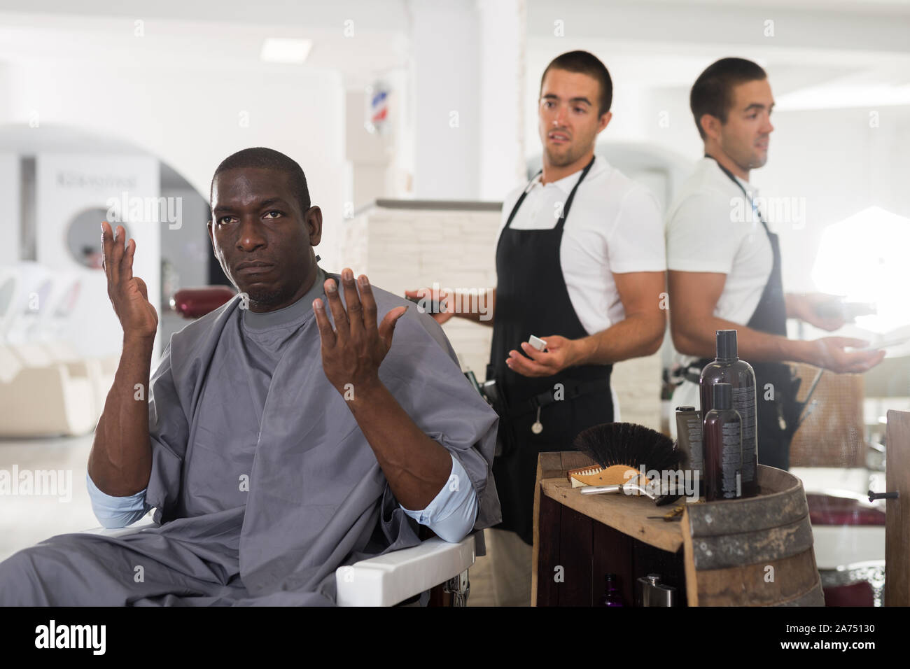 Portrait von schockiert African American in Friseur Stuhl sitzend mit verwirrten jungen Friseur hinter ihm Stockfoto