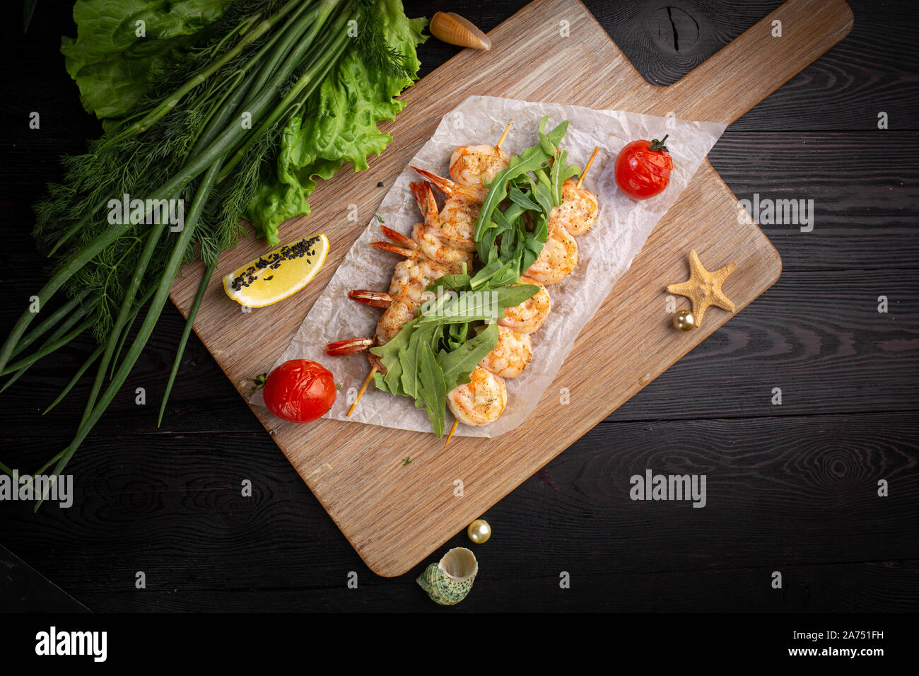 Garnelen Spieße auf einem Spieß mit Rucola, gebackene Tomaten und Zitrone auf einem Bambus Board auf einem dunklen Hintergrund Stockfoto