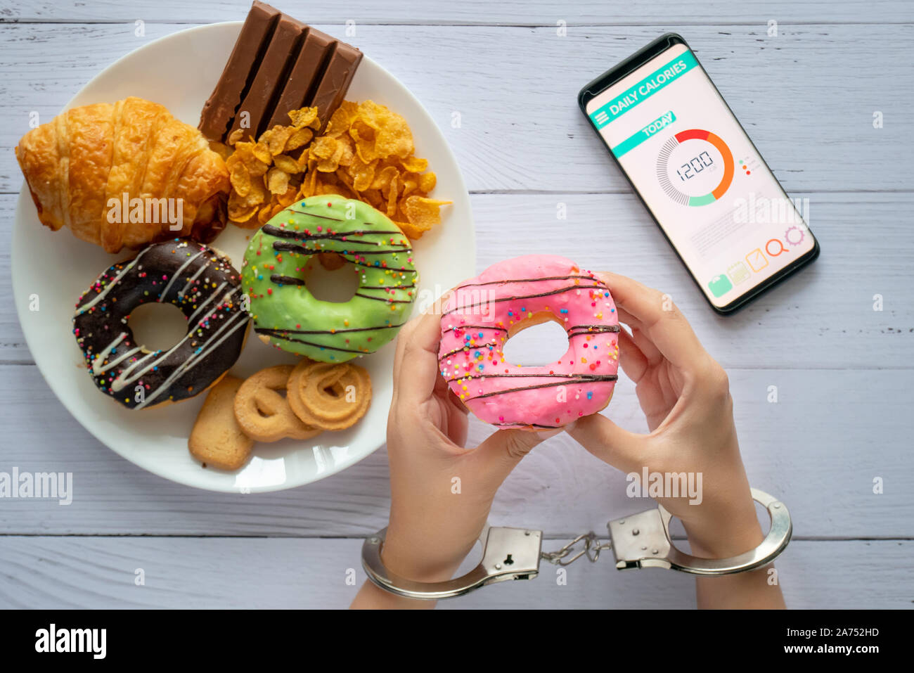 Kalorien, Ernährung und Gewichtsabnahme Konzept. nach oben Blick auf zwei Händen war Kontrolle durch Handschellen, holding Donut mit Kalorienzähler Anwendung Stockfoto