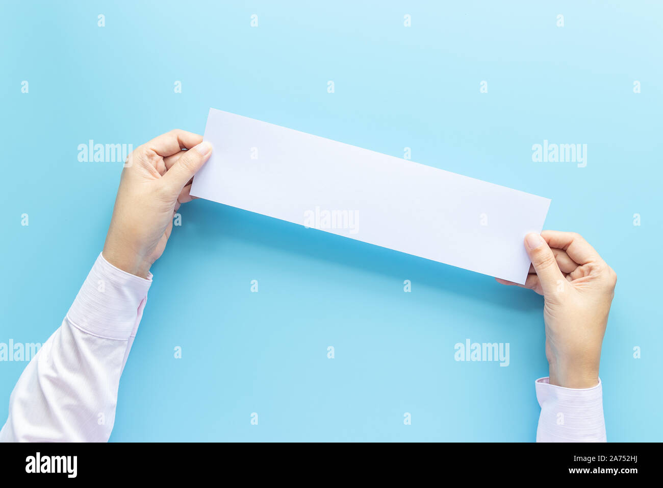 Die Hände schließen Holding leere weiße Leere horizontalen Papier Für Flyer oder Einladung mock up auf einem blauen Hintergrund. Stockfoto