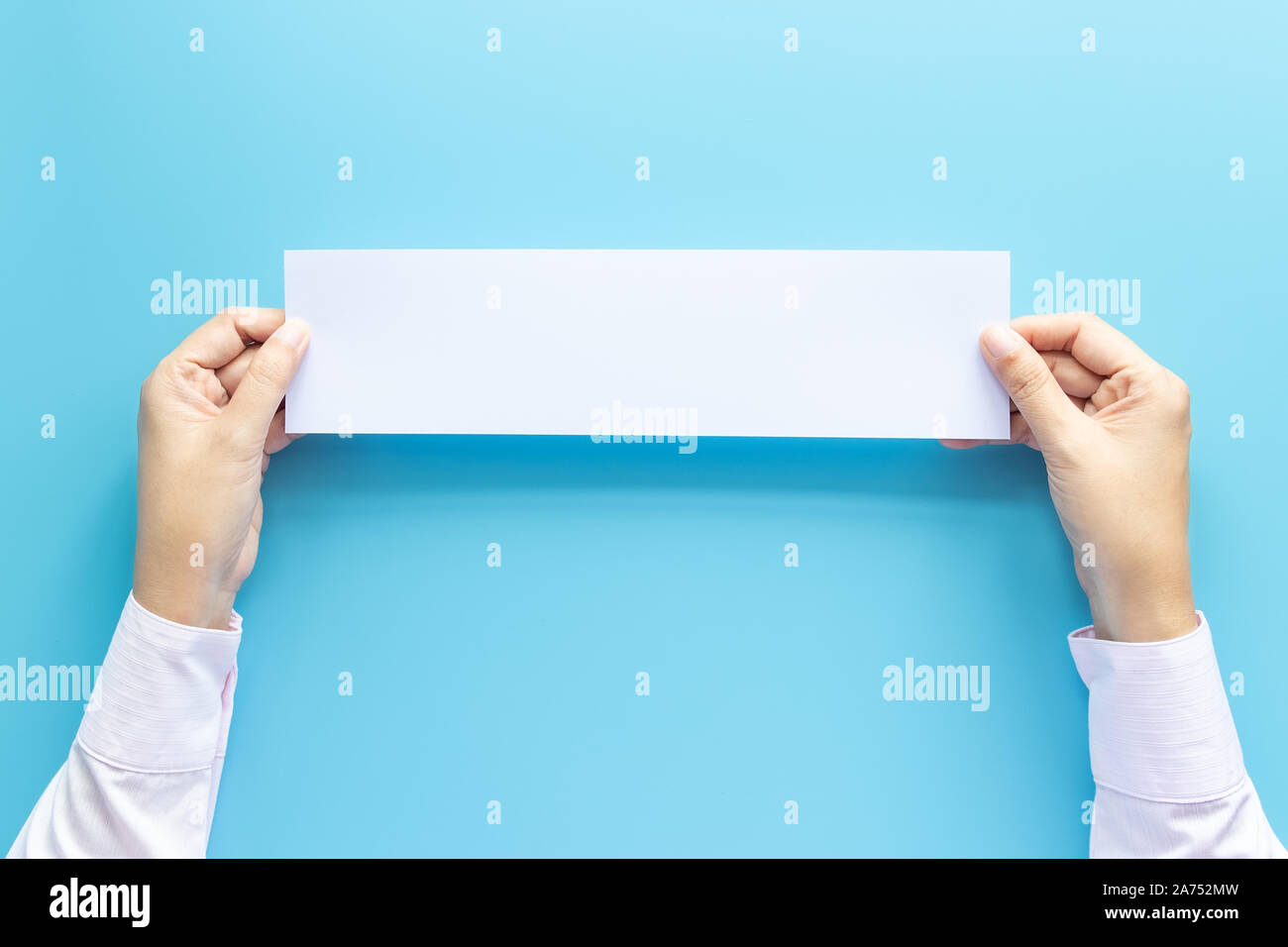 Die Hände schließen Holding leere weiße Leere horizontalen Papier Für Flyer oder Einladung mock up auf einem blauen Hintergrund. Stockfoto
