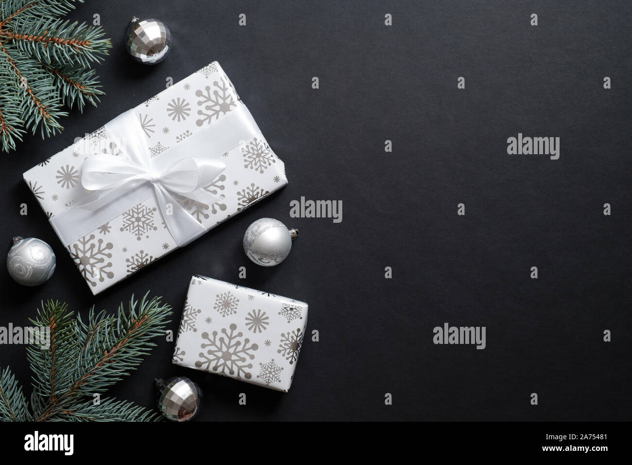 Geschenkboxen verpackt Silber Papier und Tannenbaum Äste mit dekorativen Kugeln über schwarzen Hintergrund. Weihnachten banner Mockup, Neues Jahr Postkarte Vorlage Stockfoto