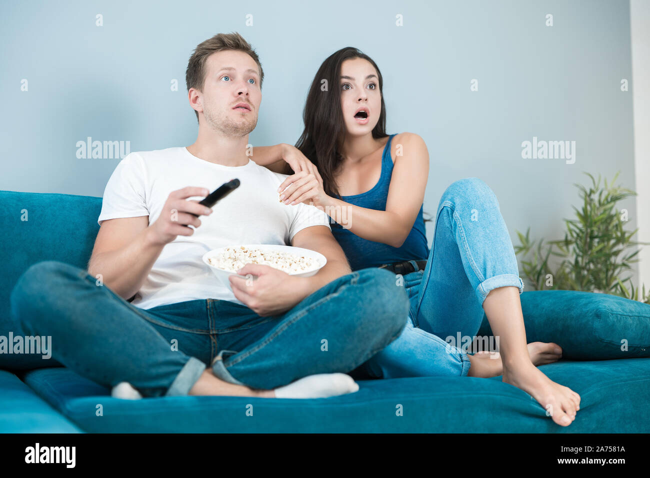 Junges Paar schöne Brünette Frau und gutaussehenden Mann beobachten Film auf dem Sofa essen Pop Corn überrascht gemütlichen Lebensstil Stockfoto