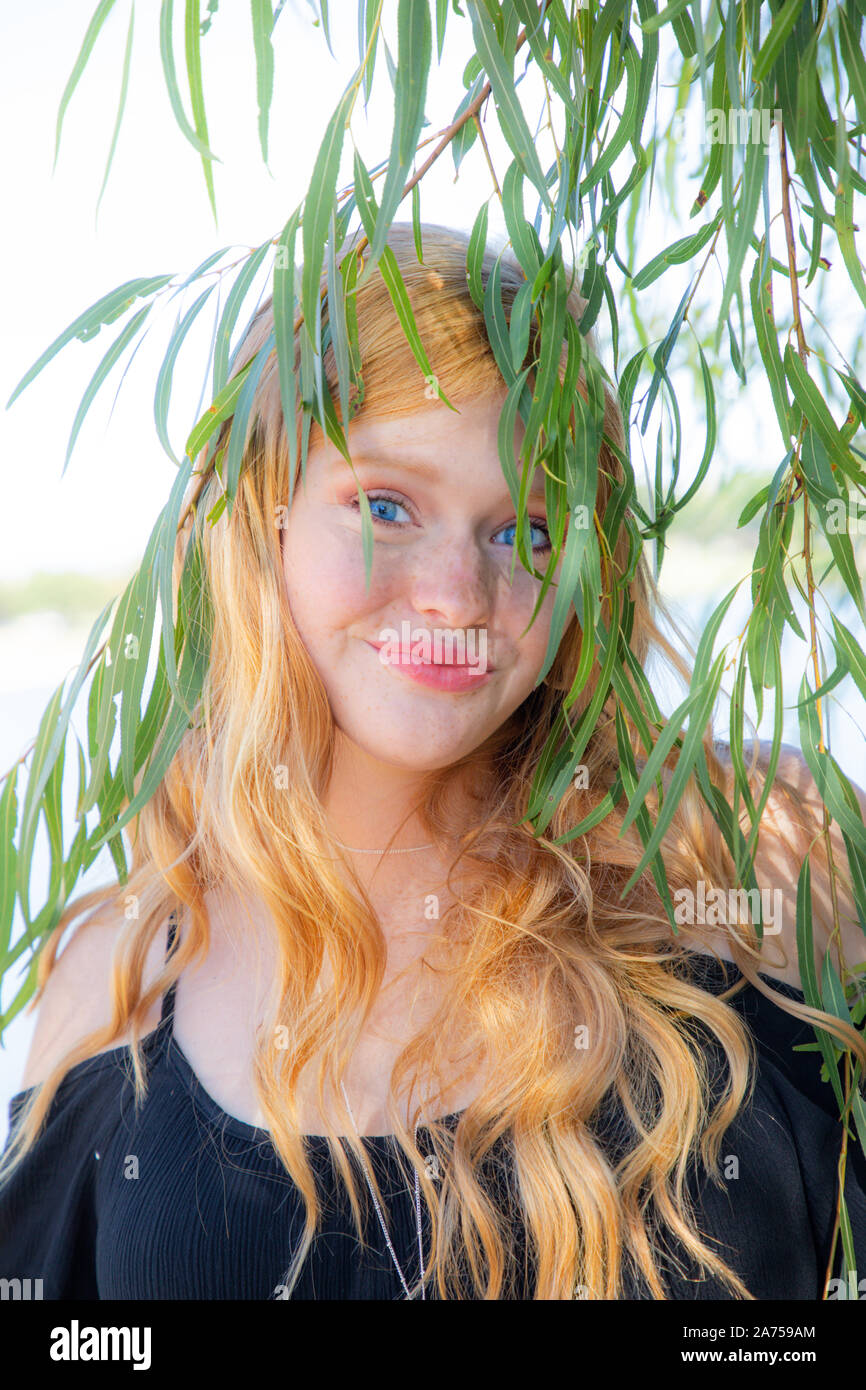 Porträt einer wunderschönen Lächeln junges Mädchen mit roten Haaren im Freien Verstecken hinter Blätter Stockfoto