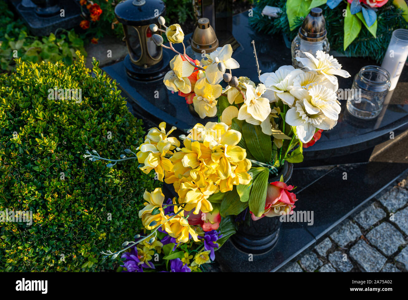 Künstliche Blumen und Kerzen liegen auf dem Grabstein auf dem Friedhof