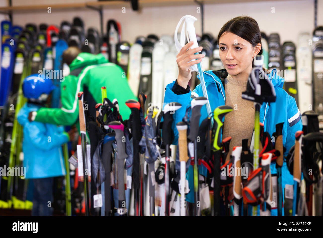 Attraktive positive Mädchen Wahl Skistöcke für Skifahren im Store von Sportgeräten Stockfoto