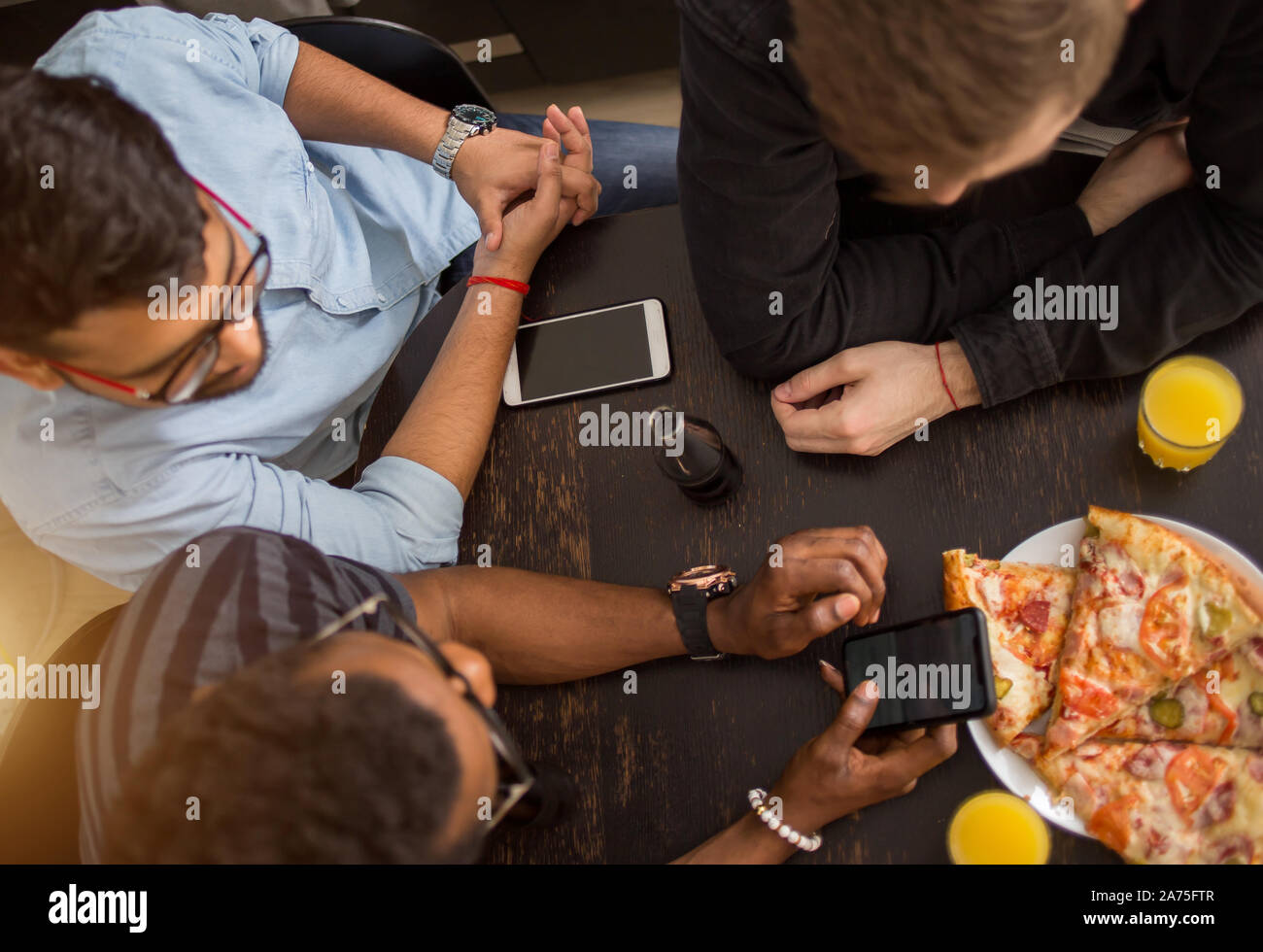 Blick von oben auf die Gruppe der multirassischen Freunde sitzen um den Tisch, Mittagessen, essen Pizza, Saft trinken, über Handy. Lieferung, Essen, Technol Stockfoto