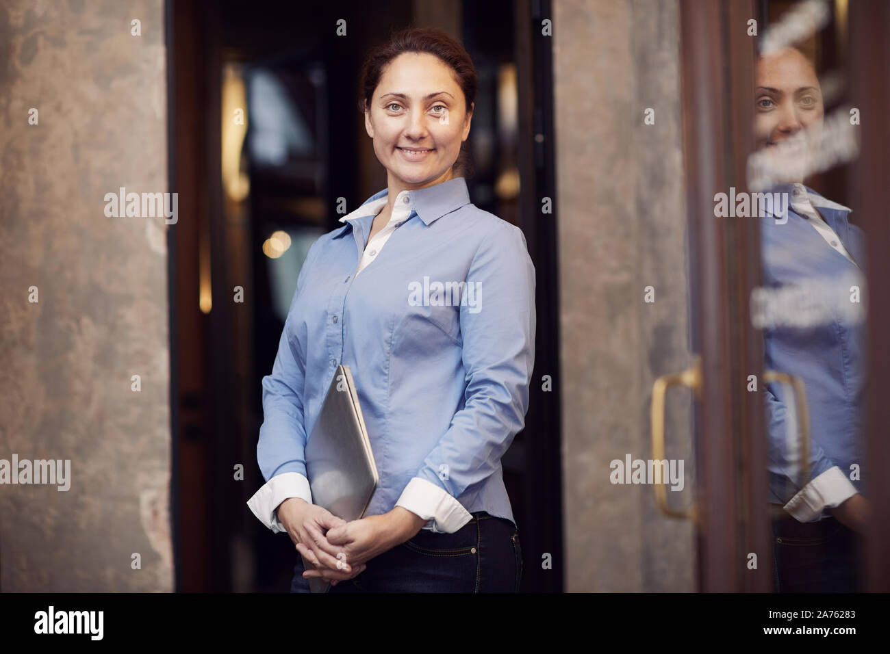 Portrait von zuversichtlich reife Geschäftsfrau im blauen Hemd holding Laptop in die Hände und lächelte Kamera im Büro Stockfoto