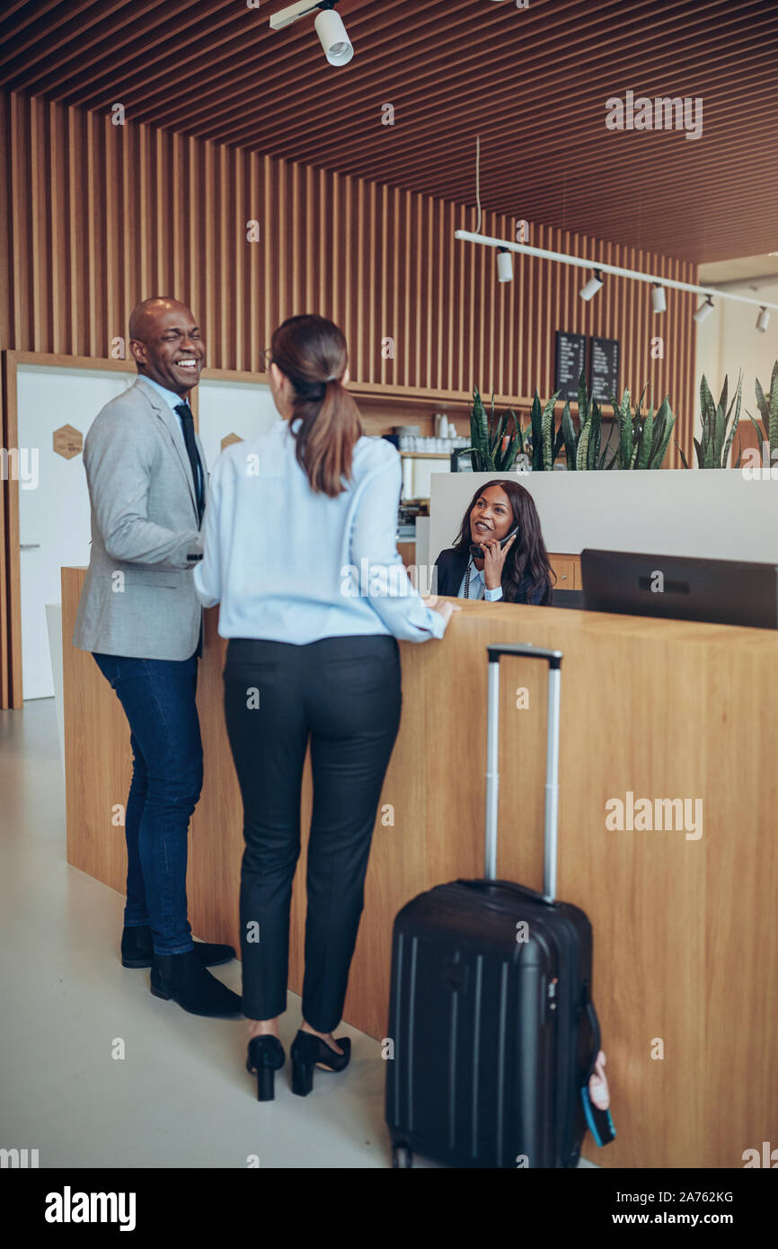 Zwei lachende Gäste ein Gespräch mit einem Concierge beim Einchecken an der Rezeption eines Hotels Stockfoto