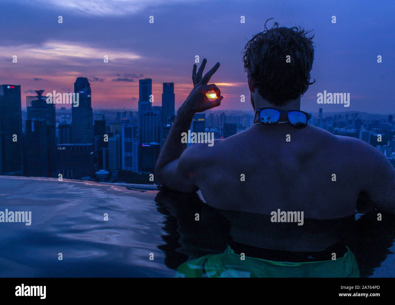 Mann im Infinity-Pool auf der Dachterrasse bei Sonnenuntergang mit Blick auf die Wolkenkratzer. Stockfoto