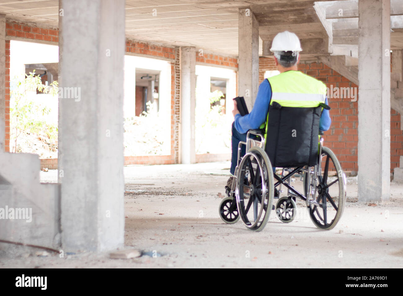 Rearvision eines Rollstuhls bau Techniker die Überwachung einer Baustelle mit Helm und Warnweste arbeiten. Behinderung Konzept Stockfoto