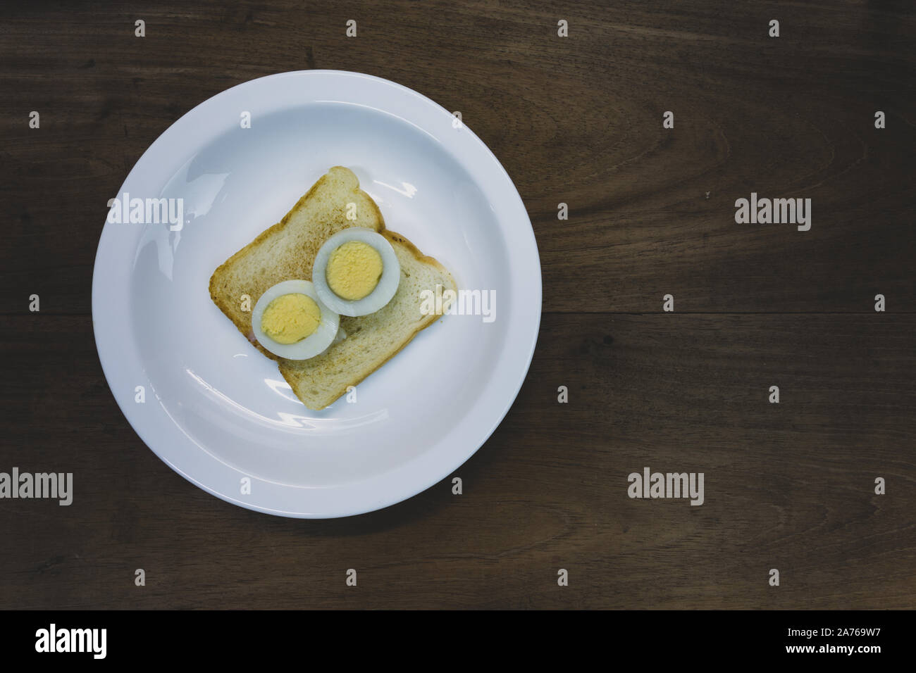 Die Hälfte geschnitten hart gekochte Ei auf getoastetes Sandwich Brot, bereit zu essen, in weiße Platte, hölzernen Tisch Hintergrund. Vintage Farben Stockfoto