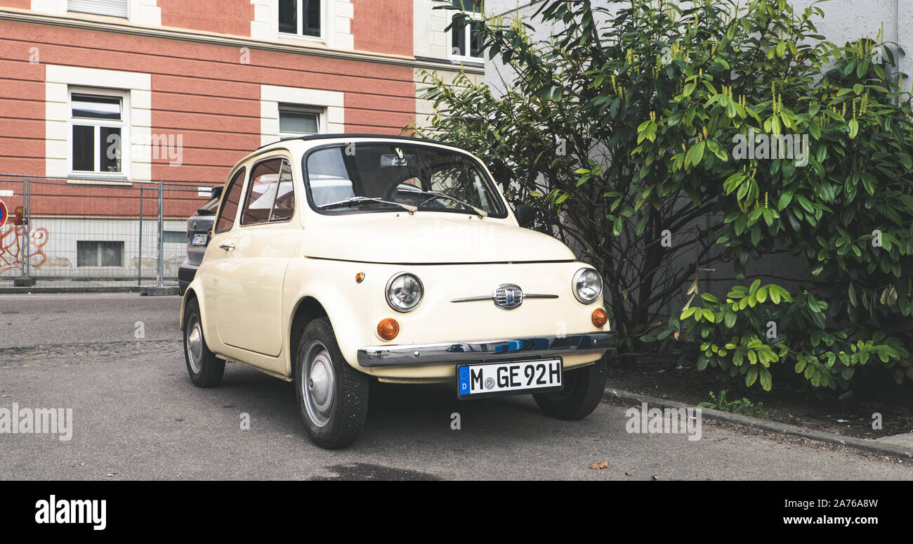 Alte Schule europäischen Auto durch eine schöne bunte Gebäude und Big Green Bush geparkt Stockfoto