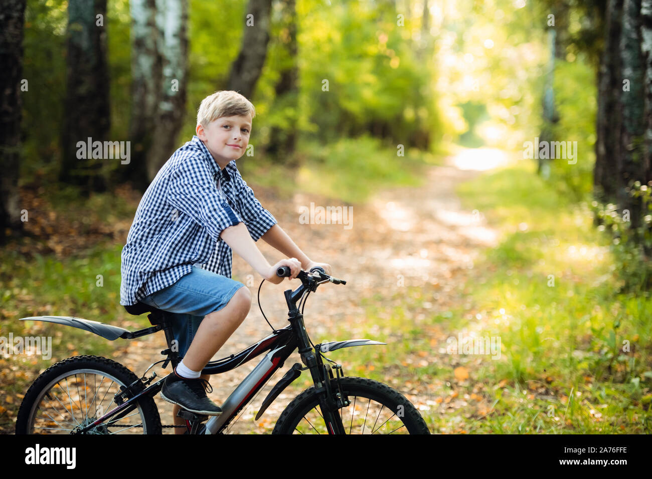 Wenig kaukasischen Boy steht in Anlehnung an das Fahrrad für die Kamera posieren. Teenager bereit Fahrrad im Park im Sommer Tag zu reiten. Wochenende Tätigkeit. Stockfoto