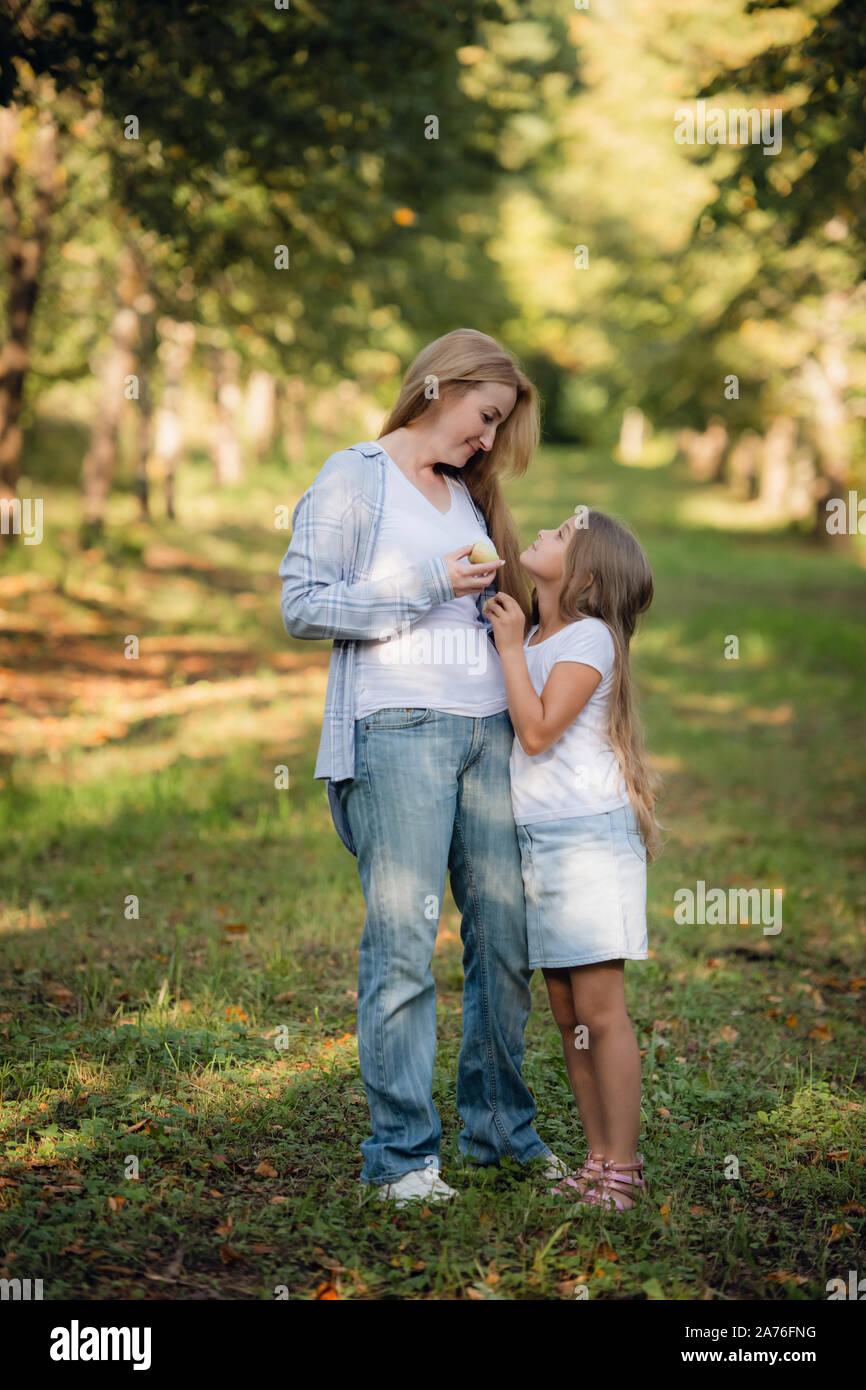 Glückliche kleine blonde Mädchen mit ihrer Mutter teilen eine Apple gerade von Apple Tree auf einem Spaziergang im Park im Sommer Stockfoto