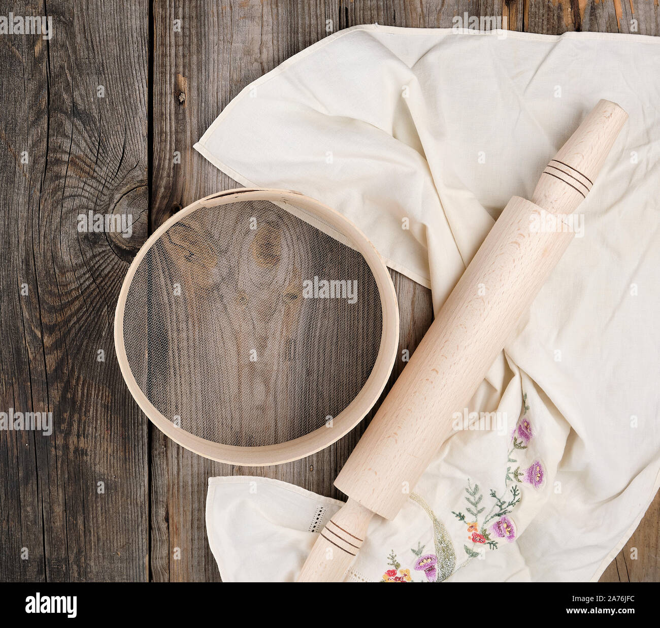 Neue Holz- Rolling Pin auf ein Textil Serviette mit Stickerei und eine runde Sieb für Mehl, grau Holz- Hintergrund Stockfoto