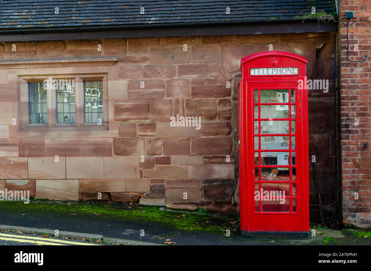 Ikonische rote Telefonbox neben einer sehr alten Steinmauer in Oulton, Staffordshire, Großbritannien. Stockfoto