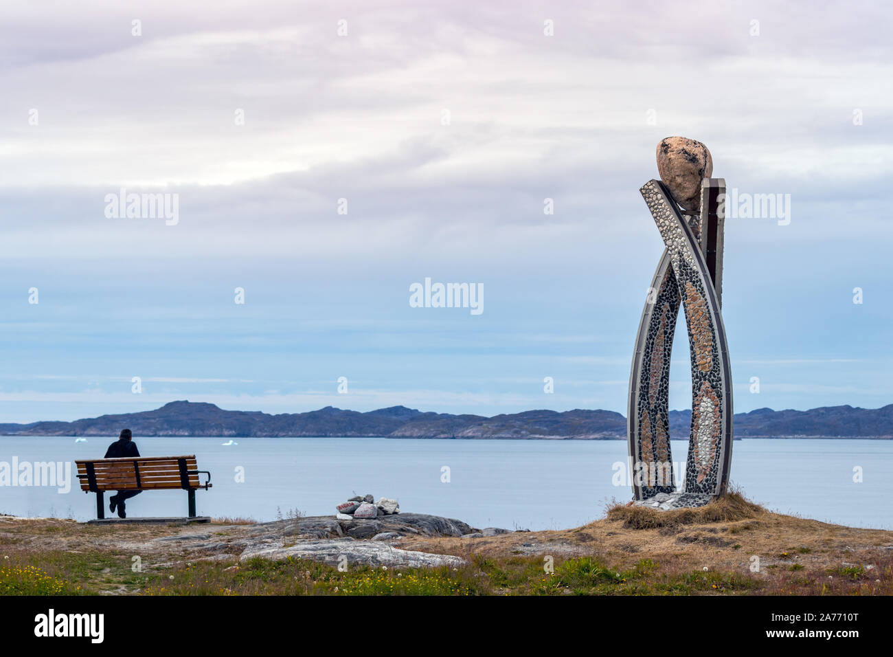 Mann sitzt auf einer Bank neben dem Inussuk Skulptur von Niels Molfedt in Westgrönland. Stockfoto