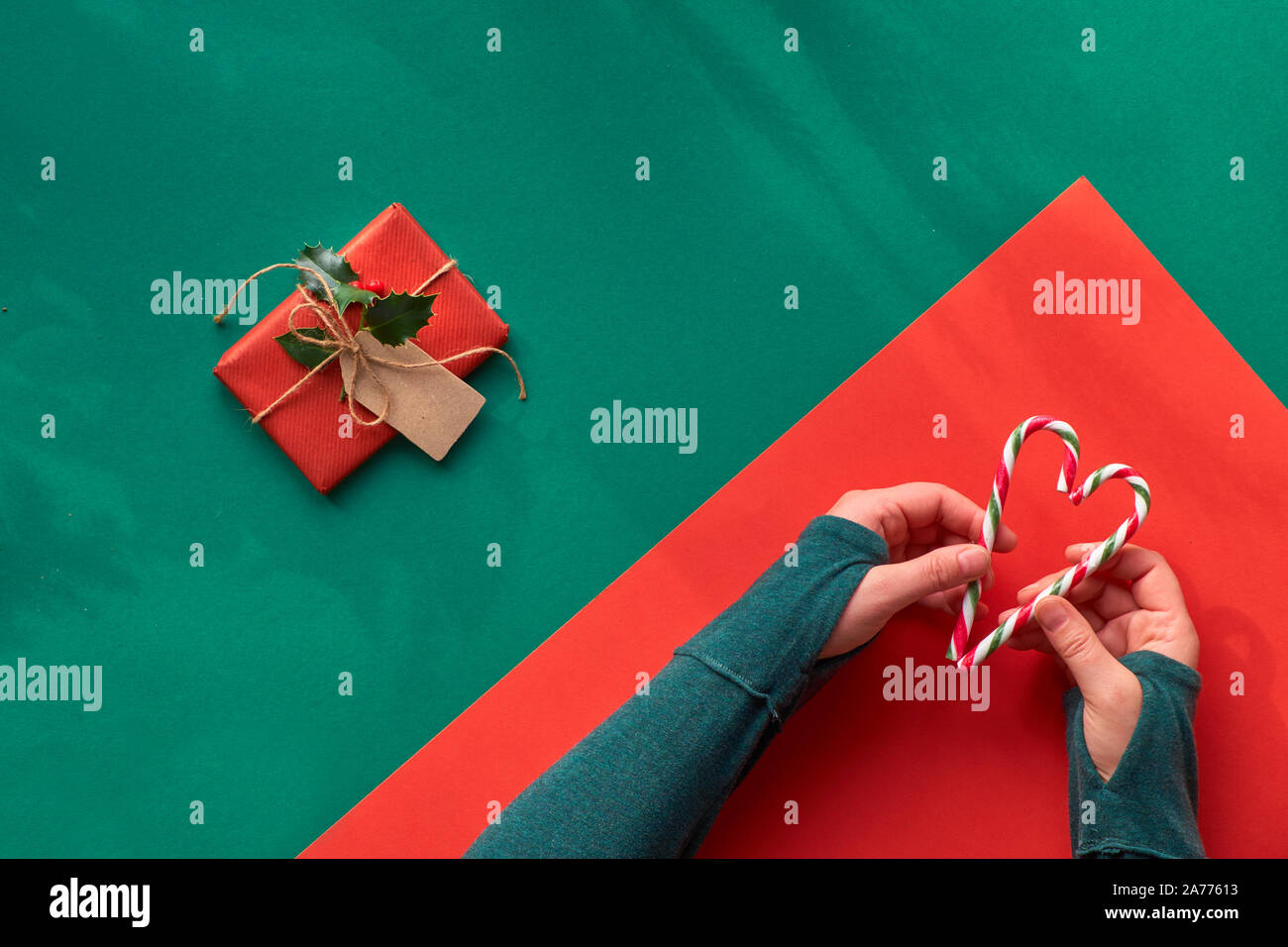 Kreative diagonal Geometrische flach an der grünen und roten Papier mit langen Schatten der Blätter. Hände in grünem t-shirt mit zwei gestreifte Zuckerstangen in Shap Stockfoto