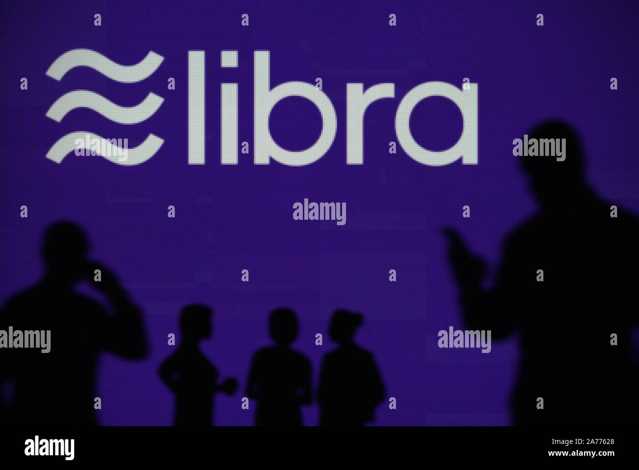 Die Libra cryptocurrency Logo ist auf einen LED-Bildschirm im Hintergrund, während eine Silhouette Person ein Smartphone verwendet (nur redaktionelle Nutzung) Stockfoto